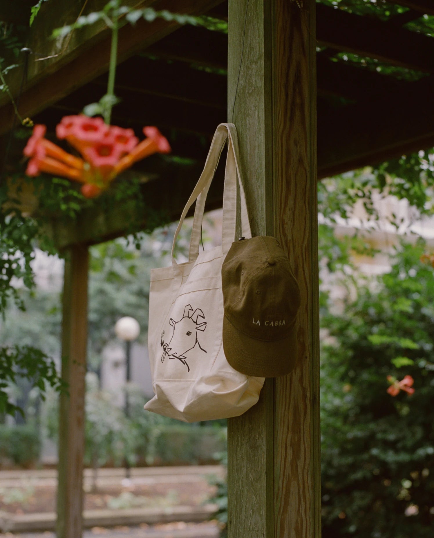 Tote bag and cap hanging on a wooden post with a garden background